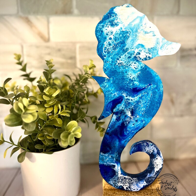 A glimpse of an ocean wave on a hand cut sea horse wooden canvas.   This is Hand cut and Hand painted wood decor.   Made and cut from aged wood; an Ocean wave fluid art is captured on this unique design.  Standing on a base with actual beach sand.
4.5â€x 12â€.   created by a local artist.