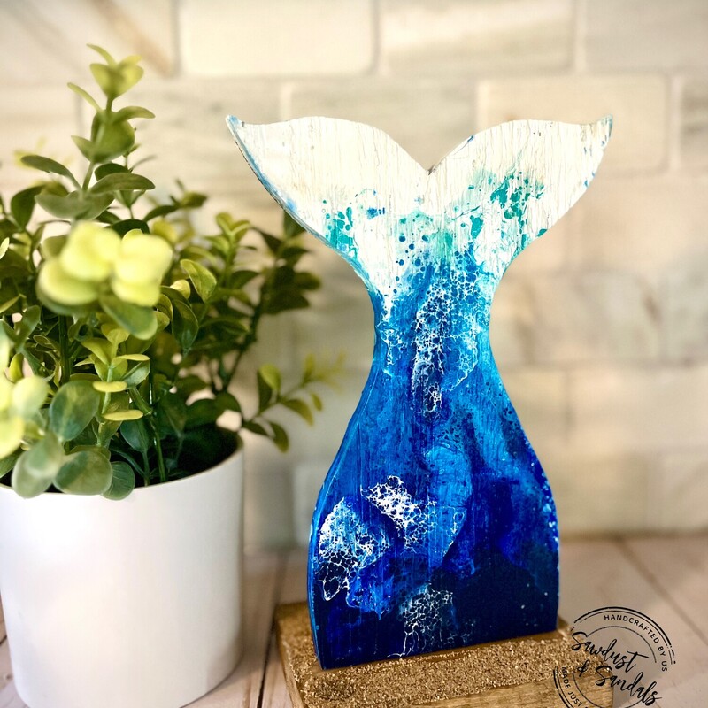 A glimpse of an ocean wave on a hand cut tail/ Fin wooden canvas.   This is Hand cut and Hand painted wood decor.   Made and cut from aged wood; an Ocean wave fluid art is captured on this unique design.  Standing on a base with actual beach sand.
6â€x9â€. created by a local artist.