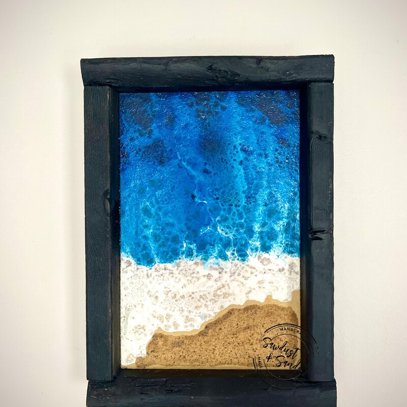 A vibrant ocean beach portrait that is hand-painted and Framed in a black wood stain.  This is a Hand cut and Hand painted wood decor item. Featuring  A vibrant Ocean wave crashing into the actual sandy  beach; using special techniques to create this image.  Colors include dark shades of blues; light blues;  turquoise and white; beach is created using actual sand. .
7â€x9â€ created by a local artist.