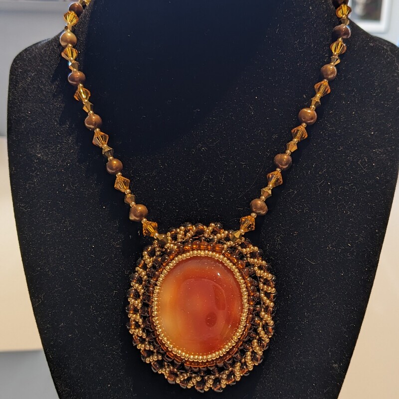 Carnelian Pearl Necklace
Jama Watts
Jewelry (Bead Embroidery)
18 in length, pendant measures 2.25 in length by 2 in wide
Large carnelain cabochon surrounded by copper and gold seed beads and strung on a chain with pearls and leaded glass crystal. Pendant is backed with tan ultrasuede.  Chain ends in a brass lobster clasp.