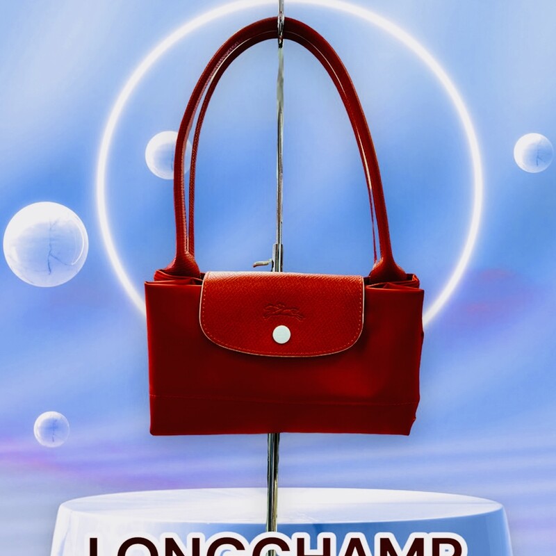 LONGCHAMP<br />
Le Pliage Tote<br />
Original Retail: $155.00<br />
<br />
Smooth, sleek red nylon and embossed leather trim make this spacious tote a no-brainer for everyday versatility and elegance.<br />
This bag is preowned, in like new conditions.  Does not appear to ever of been used.  Spotless interior and exterior.<br />
Water-resistant lining<br />
Textile with leather trim<br />
12 1/4”W x 11 3/4”H x 7 1/2”D.<br />
9\" Strap Drop<br />
*******In 1948, Jean Cassegrain turned his Paris tobacco shop—where he was known to cover his pipes in an exquisite leather—into an accessories business. Named after the famed horse track on the outskirts of Paris, Longchamp is still family owned and operated, creating superbly crafted handbags and luggage lauded for a decidedly understated, always chic look.