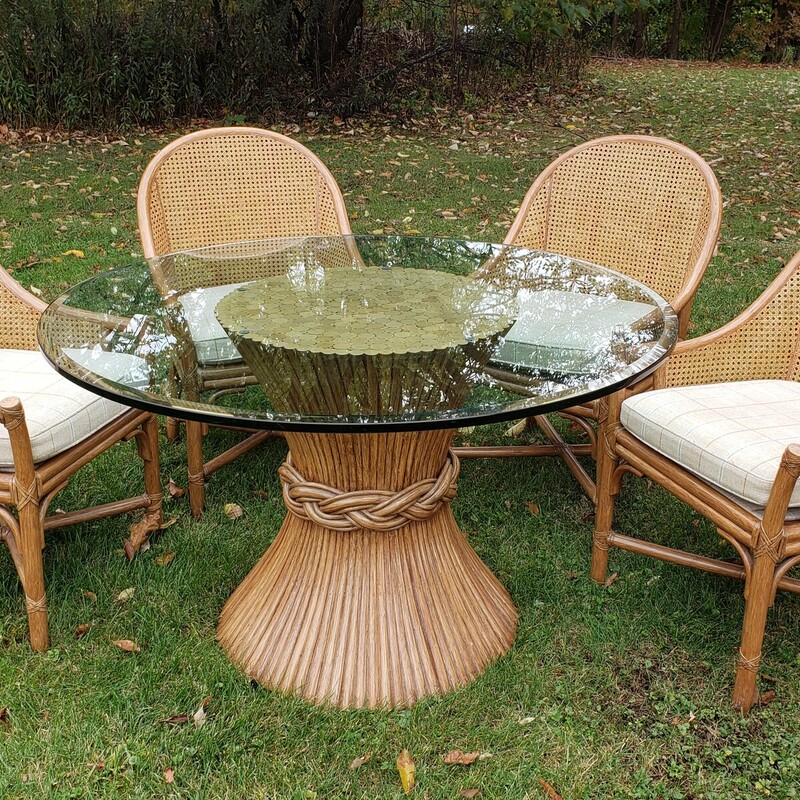 McGuire Table And Chairs. Glass top. Bamboo reed table base. With four rattan chairs with padded seats. In good condition with minimal wear.  Size: 48in in diameter. 29in tall.