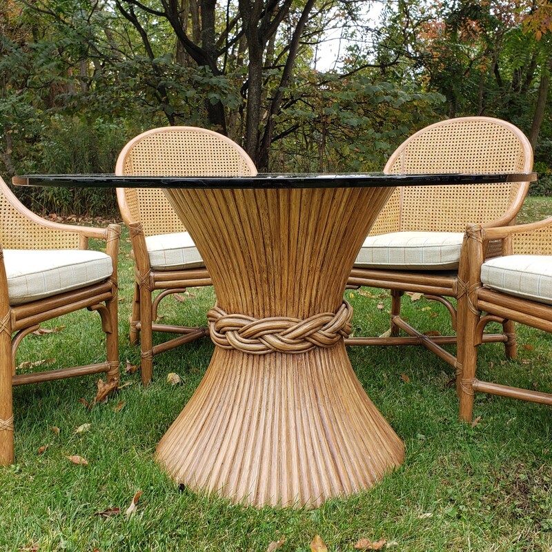 McGuire Table And Chairs. Glass top. Bamboo reed table base. With four rattan chairs with padded seats. In good condition with minimal wear.  Size: 48in in diameter. 29in tall.
