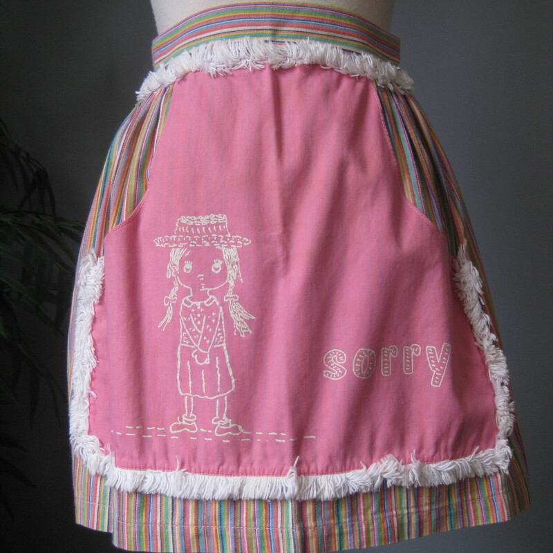 Vtg Graphic Apron, Multi, Size: None<br />
Unusual theme for a pretty apron made in the 70s of cotton.<br />
It features a sweet holly hobby like graphic with the word Sorry on the front.<br />
This graphic part is surrounded by brushy white fringe.<br />
The base of the apron is a vertical multicolor striped cotton.<br />
<br />
The apron measures 72 from end to end, the sashes are long enough to make a nice big crisp bow at the back as shown.   the body of the apron measures 16 at the waist, 29 at the bottom<br />
Thank you for looking.<br />
#66306