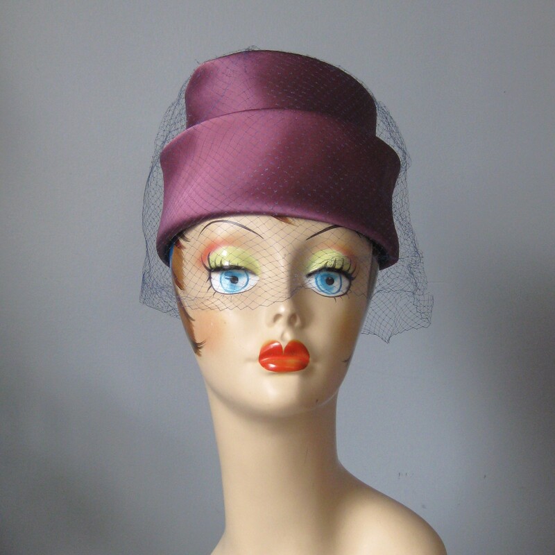 Vtg Satin Toqe, Purple, Size: None
This tailored turban style hat is chic!  It's made of a lustrous satin fabric draped and folded around a firm hat body.  It has a blue netting over over the top and sides.

It is in excellent vintage with excellent workmanship. It measures approximately 20.75 around the inside band. You might need a pin to attach it to your hair.

Please note:  my mannequin has a smaller than average head.  This hat is most likely going to sit a bit higher or further back on your head than it does on hers.

Thank you for looking.
#63063