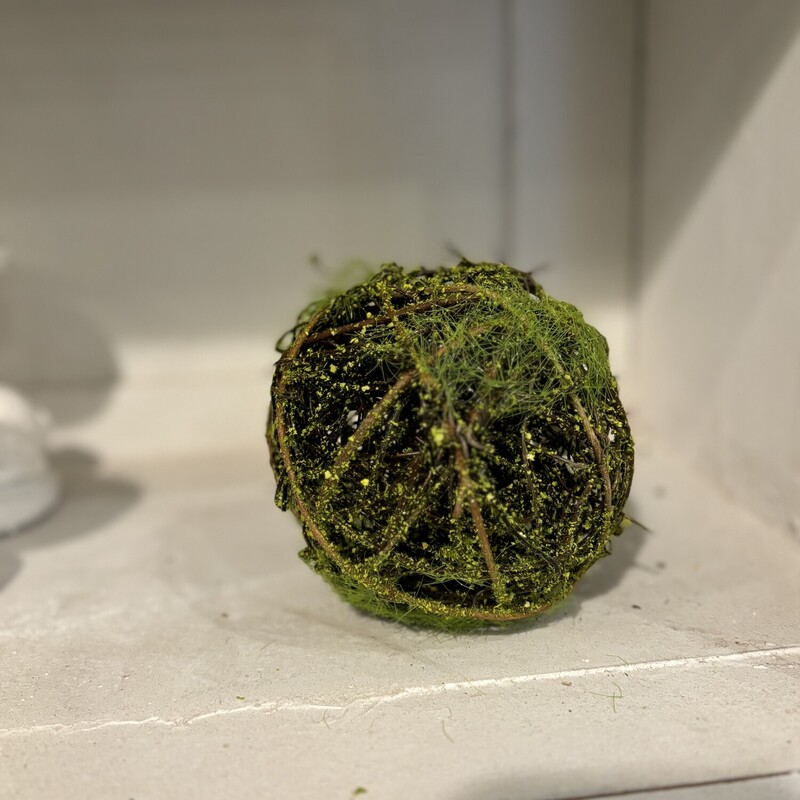 The mossy twig ball is a decorative orb made of natural brown twig material. The sphere is covered in patchy green moss detailing a woodsy look. This ball is perfect for an bowl or tray filler or on top a shelf or stack of books. Measures 6 inches in diameter