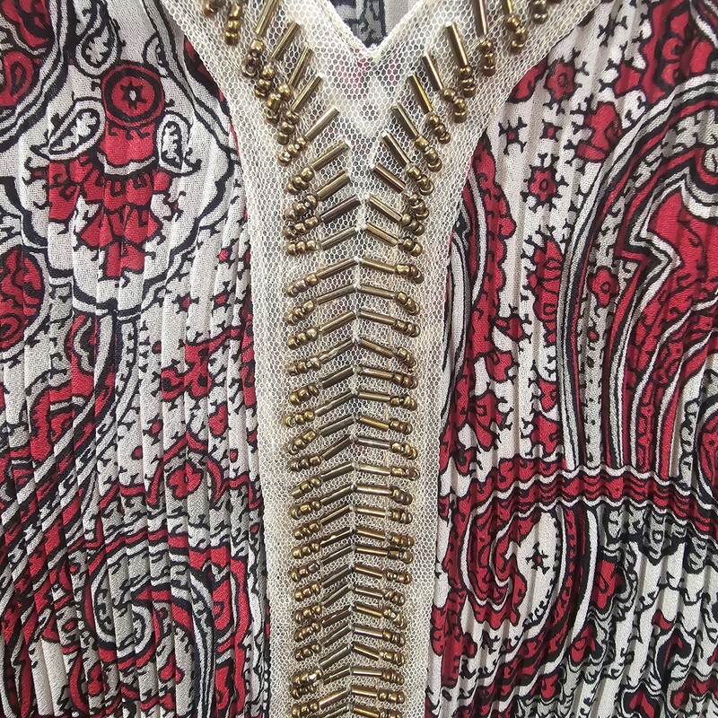 Tan colored blouse with red, black and beige print in a paisly pattern. Neck line is adorned with gold beading. Ribbed bodice allowes for extra flow. Beautiful and flattering.
