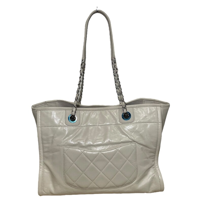 CHANEL Glazed Calfskin Small Deauville Tote in Ecru. This tote is crafted of fine glazed calfskin leather, with a Chanel advertisement logo stitched on the front, a diamond-quilted rear pocket, and caviar leather trim. The bag features leather-threaded polished silver chain link shoulder straps, and a wide top, open to a grey fabric interior with zipper and patch pockets.<br />
<br />
Date code: 22311999<br />
Year: 2016<br />
Dimnesions:<br />
Base length: 13.50 in<br />
Height: 10.00 in<br />
Width: 6.75 in<br />
Drop: 10.00 in