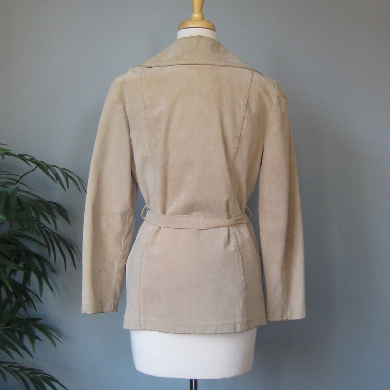 This simple hip length double breasted beige trench coat jacket has a matching belt, button closures<br />
Pockets and fully lined with a medium weight quilted fabric for a bit of warmth. (no batting)<br />
It has pretty big shoulder pads built in under the lining.<br />
<br />
it's made of pigskin which feels like a stiff-ish suede and has little marks from the hairs of the animal.<br />
This light beige coat has a couple of spots as shown and some darkened edge areas.m The gold buttons have some flaking of the finish as shown.<br />
<br />
It's marked size 12 but will NOT fit a modern size 12, better for a size 6-8<br />
Here are the flat measurements:<br />
Shoulder to shoulder: 16<br />
Armpit to armpit: 19<br />
Waist: 18<br />
Length: 27.75<br />
underarm sleeve seam: 16<br />
<br />
Thanks for looking!<br />
#69413