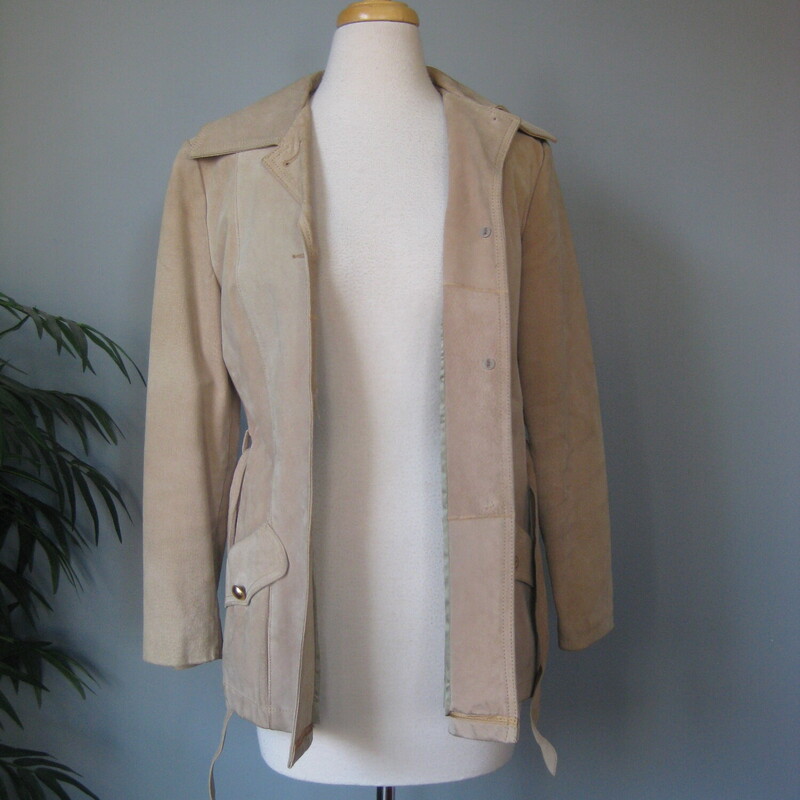 This simple hip length double breasted beige trench coat jacket has a matching belt, button closures<br />
Pockets and fully lined with a medium weight quilted fabric for a bit of warmth. (no batting)<br />
It has pretty big shoulder pads built in under the lining.<br />
<br />
it's made of pigskin which feels like a stiff-ish suede and has little marks from the hairs of the animal.<br />
This light beige coat has a couple of spots as shown and some darkened edge areas.m The gold buttons have some flaking of the finish as shown.<br />
<br />
It's marked size 12 but will NOT fit a modern size 12, better for a size 6-8<br />
Here are the flat measurements:<br />
Shoulder to shoulder: 16<br />
Armpit to armpit: 19<br />
Waist: 18<br />
Length: 27.75<br />
underarm sleeve seam: 16<br />
<br />
Thanks for looking!<br />
#69413