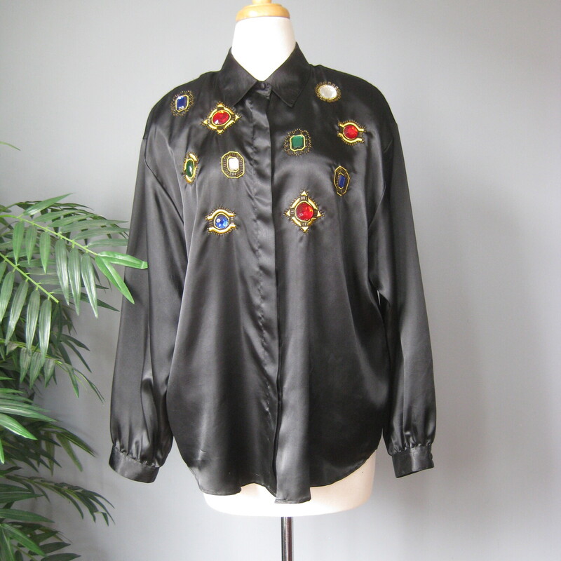 This long sleeved black satin blouse sports large metal set plastic jewels.
It's such an 80s iconic piece!
by Laura & Jayne Collection.  Buttons up the front in a hidden button placket
BIG shoulder pads
Curved hem
button cuffs
This would fit  a modern medium generously, or a large
Here are the flat measurements, please double where appropriate:
Shoulder to shoulder: 20
Armpit to Armpit: 22.5
Width at hem: 23
Underarm sleeve seam: 17.5
Length: 29.5

Excellent vintage condition
Thank you for looking.
#67875