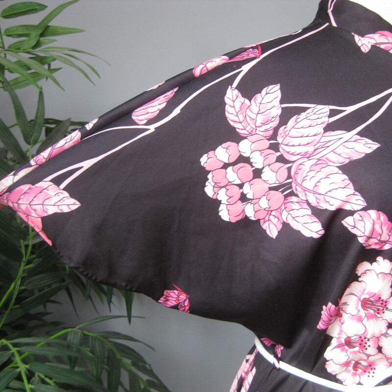 Pretty floral top with a black background and large pink flowers<br />
no tags or labels but it is made with nylon knit, with some stretch.<br />
It has a slit at the neckline with a single button<br />
It has wide cut on sleeves, slits at the end of the side seams, and a pocket on one side.<br />
Comes with a matching cord belt in white<br />
pulls on over the head.<br />
it will serve as a cute top, a VERY short dress or beach coverup or a short robe.<br />
<br />
<br />
Here are the flat measurements, please double where appropriate:<br />
<br />
Armpit to armpit: 21.5<br />
waist area: 20<br />
hip area: 21<br />
Length: 34<br />
slits: 4.5<br />
<br />
Excellent vintage condition.<br />
<br />
Thanks for looking!<br />
#71620