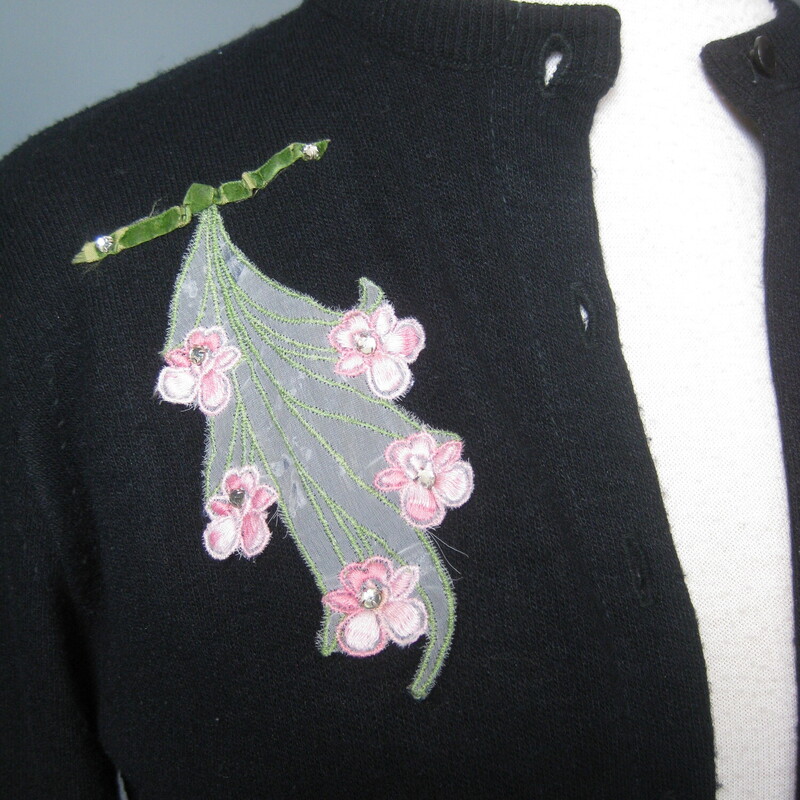 HI Sweater Girl, This adorable sweater from the late 50s early 60s in black features decorative embellishment. a bit of applied gauze with teeny green and pink fabric flowers and a few rhinestones.<br />
It's by Browser<br />
Condition: Good condition, it's been well loved and the knit and the label shows it. no holes, major pilling, stains. Price accordingly.<br />
<br />
Flat measurements, please double where appropriate:<br />
Shoulder to Shoulder: 15.5<br />
Armpit to Armpit: 18.75<br />
Width at bottom: 14<br />
length: 20<br />
Underarm sleeve seam length: 15.25<br />
<br />
Thanks for looking!<br />
#73085