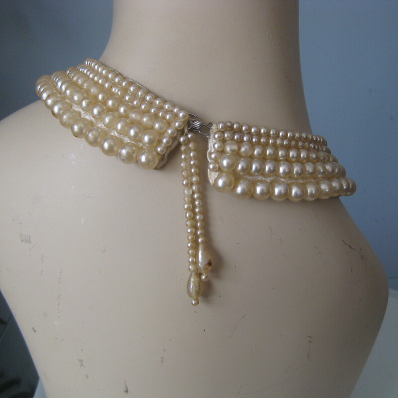 Pearl Collar, White, Size: None
This is a pretty faux pearl collar from the 1950s, it is fabric backed and has pretty dangly strings of pearls  at the ends where there is a hook and eye closure.

These chokers look amazing on modern girls and would make a great vintage gift.
15.5 end to end

This one is in fair condition and is priced accordingly.
The finish has rubbed off on some of the pearls, especially the dangly ones at the back. There is a one inch section at one edge that is missing pearls
Still totally wearable and pretty.
Thanks for looking.
#50952