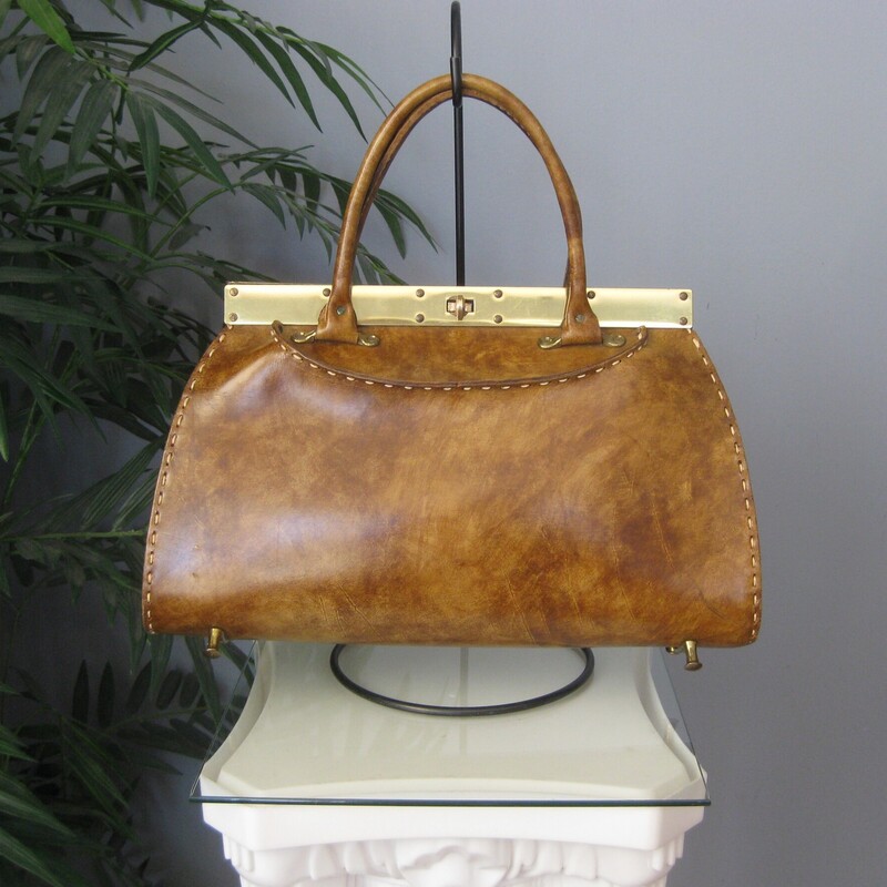 Vtg Manler Cali Structure, Brown, Size: None
Roomy leather handbag with high end Western Style.  Made in California by Mahler.
It's hard smooth glossy leather with sculpturing shaping at the top, light brown, tan in color with white top stitching.
Strong gold hardware lines the top edge.
It has a pass through clasp and unique brass feet that resemble the pommels of western saddles.
Rawhide interior with a slip pocket made of vinyl.
Amazing condition,
The gold marking inside is partially worn away

Measurements:
Width: 15.5
Height: 9.5
Depth at bottom: 3.75
Handle Drop: 4.75

Thanks for looking!
#78852