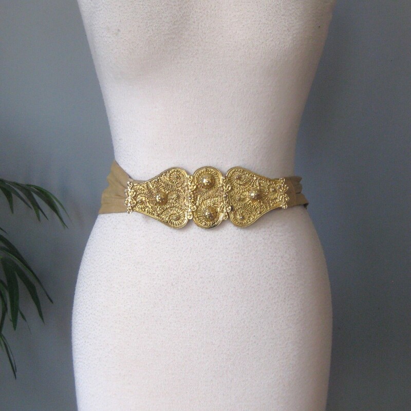 From the power days of the later 80s/early 90s comes this gorgeous gold metal and taupe leather belt by Morris Moskowitz<br />
The belt clasps in the front and is made of heavy gold covered metal with an exotic somewhat brutalist high relief motif.<br />
Excellent condition with a little rub off of the gold on the higher parts of the the modling.<br />
The leather has some marks and age.<br />
The belt can be adjusted a bit smaller or larger.<br />
Length of belt (including buckle): 29 as shown<br />
<br />
Thanks for looking!<br />
#78416