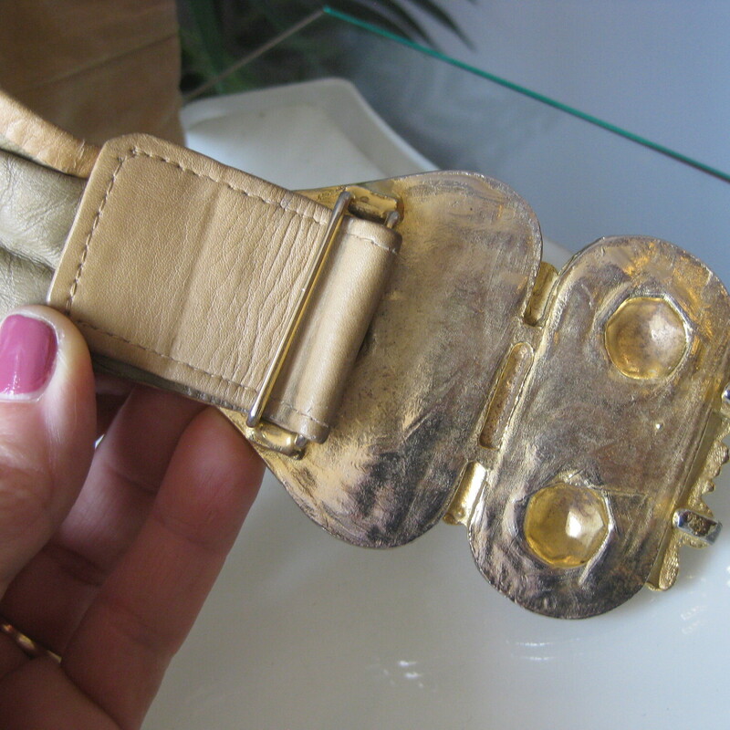 From the power days of the later 80s/early 90s comes this gorgeous gold metal and taupe leather belt by Morris Moskowitz<br />
The belt clasps in the front and is made of heavy gold covered metal with an exotic somewhat brutalist high relief motif.<br />
Excellent condition with a little rub off of the gold on the higher parts of the the modling.<br />
The leather has some marks and age.<br />
The belt can be adjusted a bit smaller or larger.<br />
Length of belt (including buckle): 29 as shown<br />
<br />
Thanks for looking!<br />
#78416