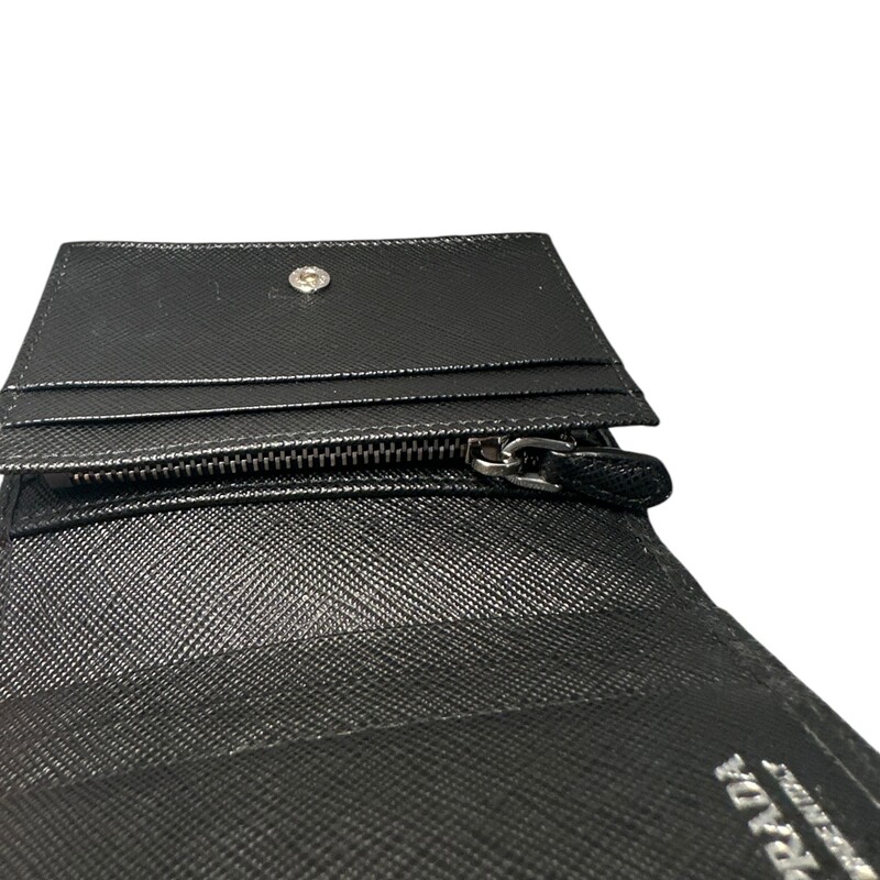 Prada Saffiano Black Compact Wallet<br />
Saffiano leather wallet with enameled metal triangle logo expresses sleek elegance. The accessory with clean lines has a zipper coin compartment, bill compartment, and five card slots.<br />
Snap fastener<br />
Enameled metal triangle logo<br />
One bill compartment<br />
Four card slots<br />
Two internal pockets<br />
Internal coin pocket with zipper<br />
Dimension: 8.5'' W x 11.2'' H