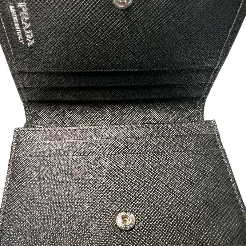 Prada Saffiano Black Compact Wallet<br />
Saffiano leather wallet with enameled metal triangle logo expresses sleek elegance. The accessory with clean lines has a zipper coin compartment, bill compartment, and five card slots.<br />
Snap fastener<br />
Enameled metal triangle logo<br />
One bill compartment<br />
Four card slots<br />
Two internal pockets<br />
Internal coin pocket with zipper<br />
Dimension: 8.5'' W x 11.2'' H