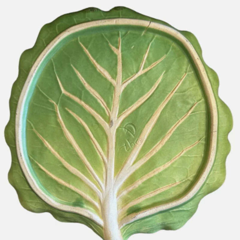 Patricia Garrett Cabbage Lettuce Plate
Green Tan Pottery
Size: 8x9H
This stunning plate by Patricia Garrett is a true work of art. The cabbage leaf/lettuce leaf shape is beautifully crafted with a matte green finish. The plate is 8 7/8 in diameter and 7/8 in height, with a width of 8 1/8. It is an original, handmade piece of ceramic that is perfect for all occasions.The plate is part of the Vegetable Art Pottery product line and was produced in the late 20th century in the United States. It features an incised backstamp.
Matching Plates Sold Separately