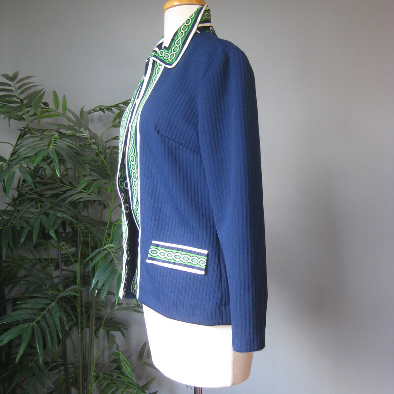 Here's a topper for someone who loves retro style. This big shirt or open cardigan is made of poly double knit, sturdy and pretty warm, washer and dryer safe. It's blue with green and white geometric contrast trim.<br />
It has decorative pocket flaps on the front (no working pockets) and a single hook and eye closure at the neck.<br />
Unlined<br />
No tags<br />
A little bit of stretch<br />
<br />
Here are the flat measurements, please double where appropriate:<br />
<br />
Shoulder to shoulder: 16<br />
armpit to armpit: 20<br />
Length: 24.75<br />
<br />
Thanks for looking!<br />
#73285