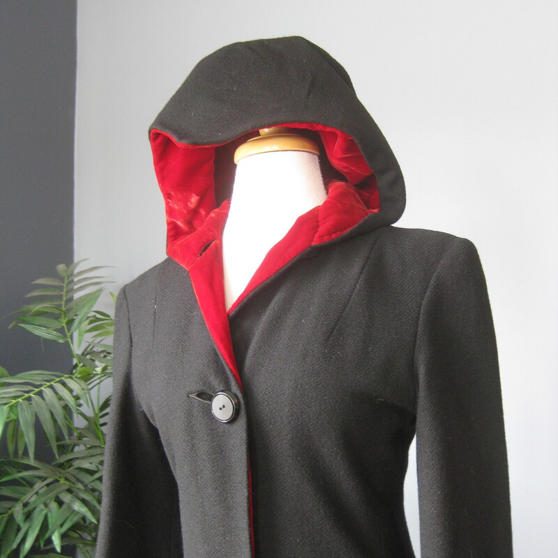 Long and Slim Black Wool coat with a hood.<br />
Romantic and striking!<br />
Seems to have been handmade.<br />
The hood and front facing is lined with red velvet.<br />
The body of the coat has a warm interlining and another orange lining next to the body.<br />
Button Closure<br />
It's quite small.  Made for a teenager's body.  My mannequin fits a modern size 4 nicely.  This coat does button up on my mannequin but it is too snug for practical purposes.<br />
Here are the flat measurements, please double where appropriate:<br />
Shoulder to shoulder: 17<br />
Armpit to armpit: 18<br />
Waist: 14.75<br />
Hip: 19.5<br />
Underarm sleeve seam length: 16<br />
Length: 55.5  This might be long for your teen but it wouldn't be too hard to take it up.<br />
Excellent condition  The only flaw is some stains on one part of the orange lining as shown.<br />
Thanks for looking!<br />
#82459