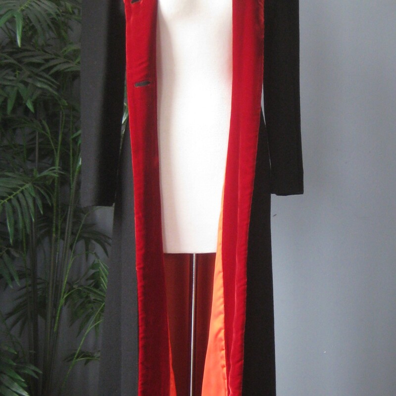 Long and Slim Black Wool coat with a hood.<br />
Romantic and striking!<br />
Seems to have been handmade.<br />
The hood and front facing is lined with red velvet.<br />
The body of the coat has a warm interlining and another orange lining next to the body.<br />
Button Closure<br />
It's quite small.  Made for a teenager's body.  My mannequin fits a modern size 4 nicely.  This coat does button up on my mannequin but it is too snug for practical purposes.<br />
Here are the flat measurements, please double where appropriate:<br />
Shoulder to shoulder: 17<br />
Armpit to armpit: 18<br />
Waist: 14.75<br />
Hip: 19.5<br />
Underarm sleeve seam length: 16<br />
Length: 55.5  This might be long for your teen but it wouldn't be too hard to take it up.<br />
Excellent condition  The only flaw is some stains on one part of the orange lining as shown.<br />
Thanks for looking!<br />
#82459