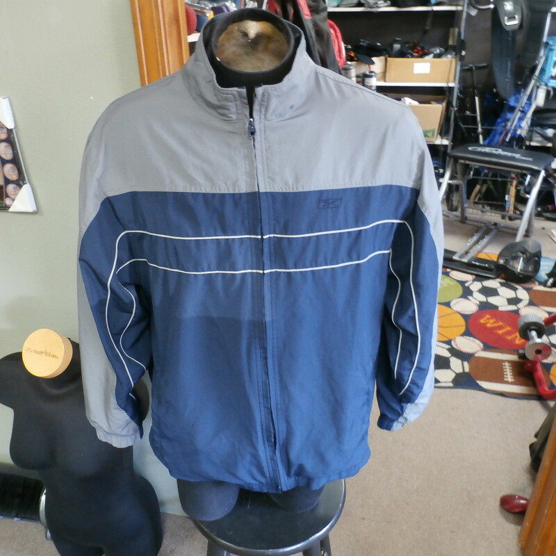 Title: reebok men's zip up jacket blue Large #22940
Our Clothes Rating: 3- Good Condition
Brand: Reebok
size: Men's Large- (Waist: 24\" Length: 28\")
color: Blue and gray
Style: zip up jacket; mock neck
Condition: 3 - Good - wrinkled; minor fading and discoloration; small burn hole on the front near the pocket; minor snags throughout; noticeable heavy pilling on the lining; overall worn looking
Shipping: FREE
Item #: 22940