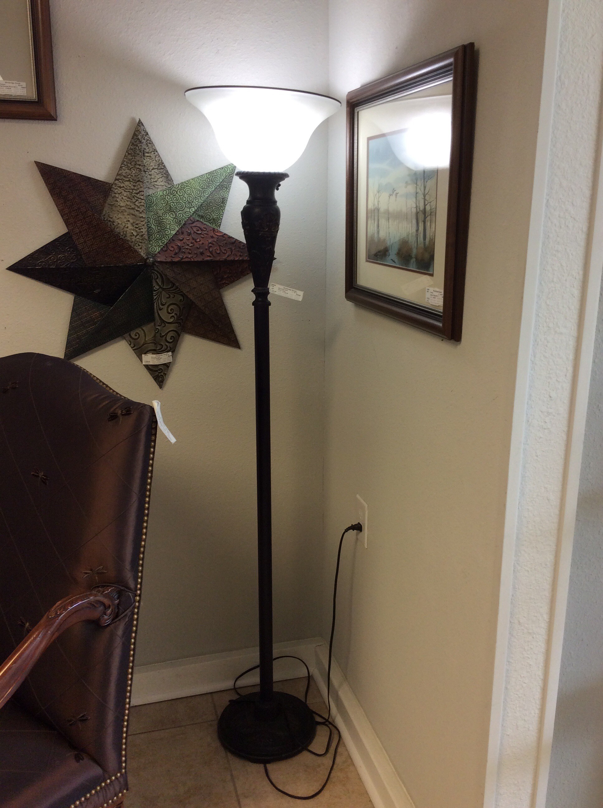 This floor lamp features a tall, slim black base with vintagy embellishments and a white uplight.