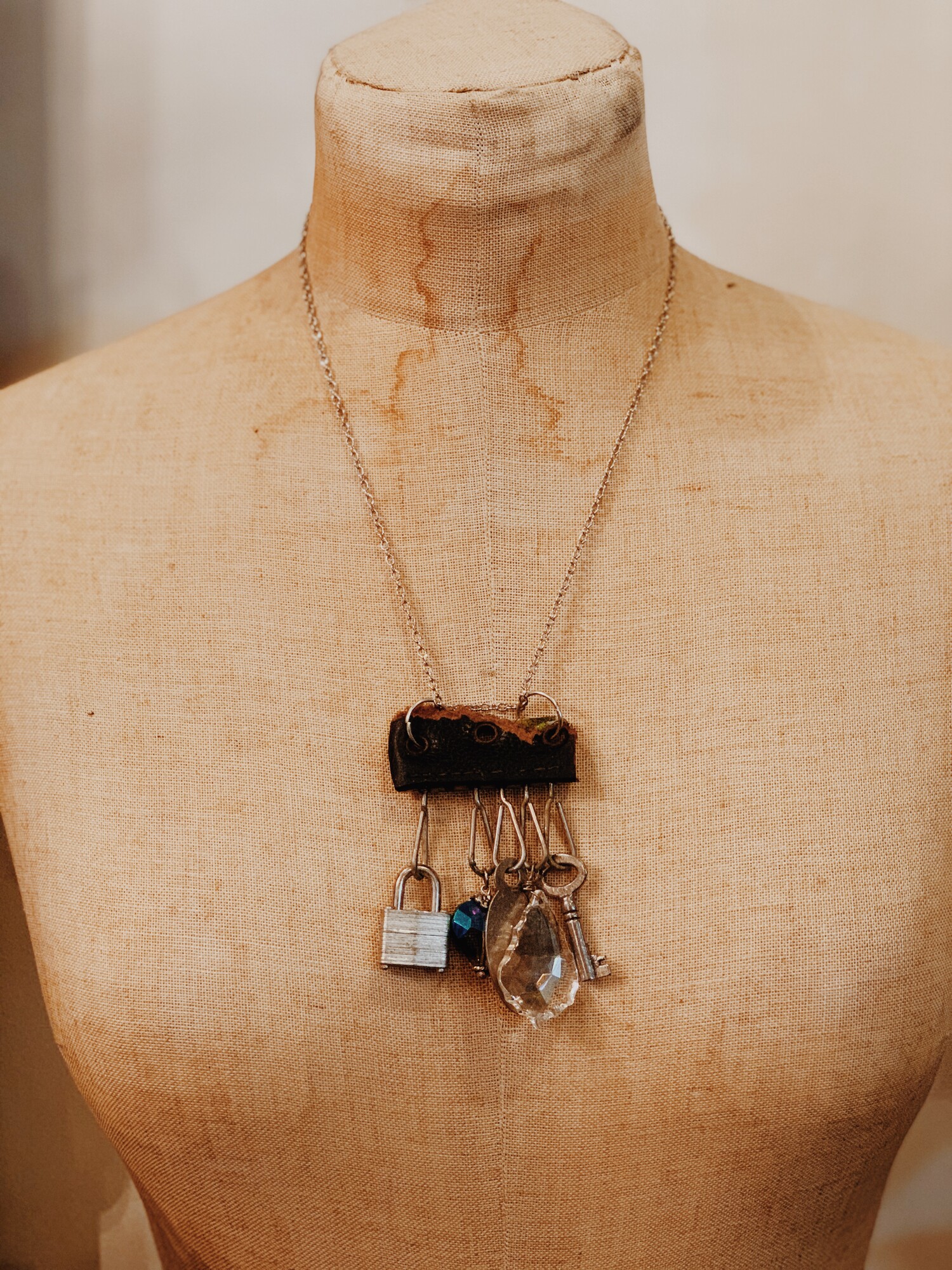 This one of a kind, handmade necklace is perfect for those who love unique! Hanging from leather is a padlock, a key, a crystal, a heart charm, and a silver tag. It is on a 20 inch chain.