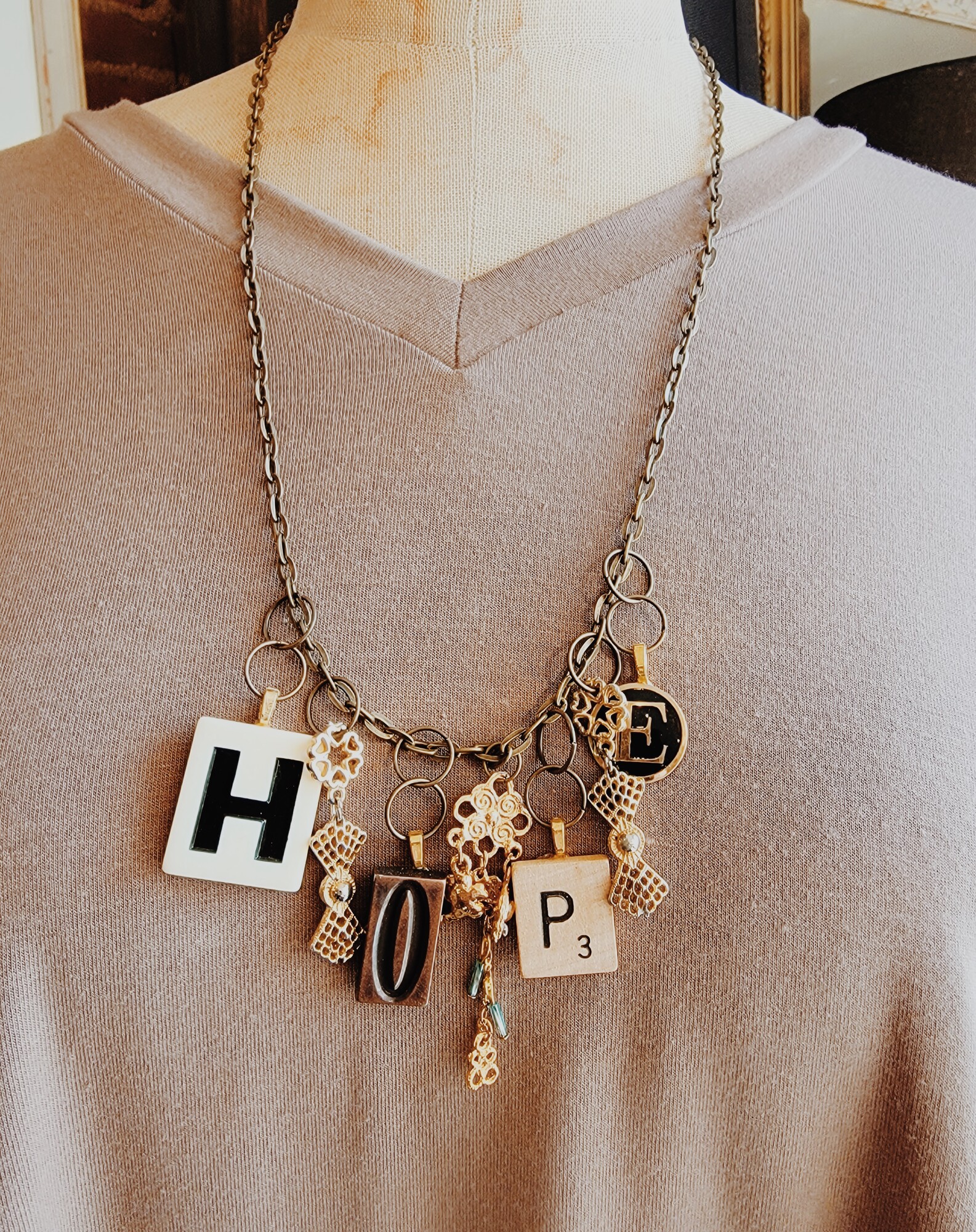 This beautiful necklace is on a 25 inch chain and spells out hope in game pieces! Also hanging from the chain are a variety of gold charms.