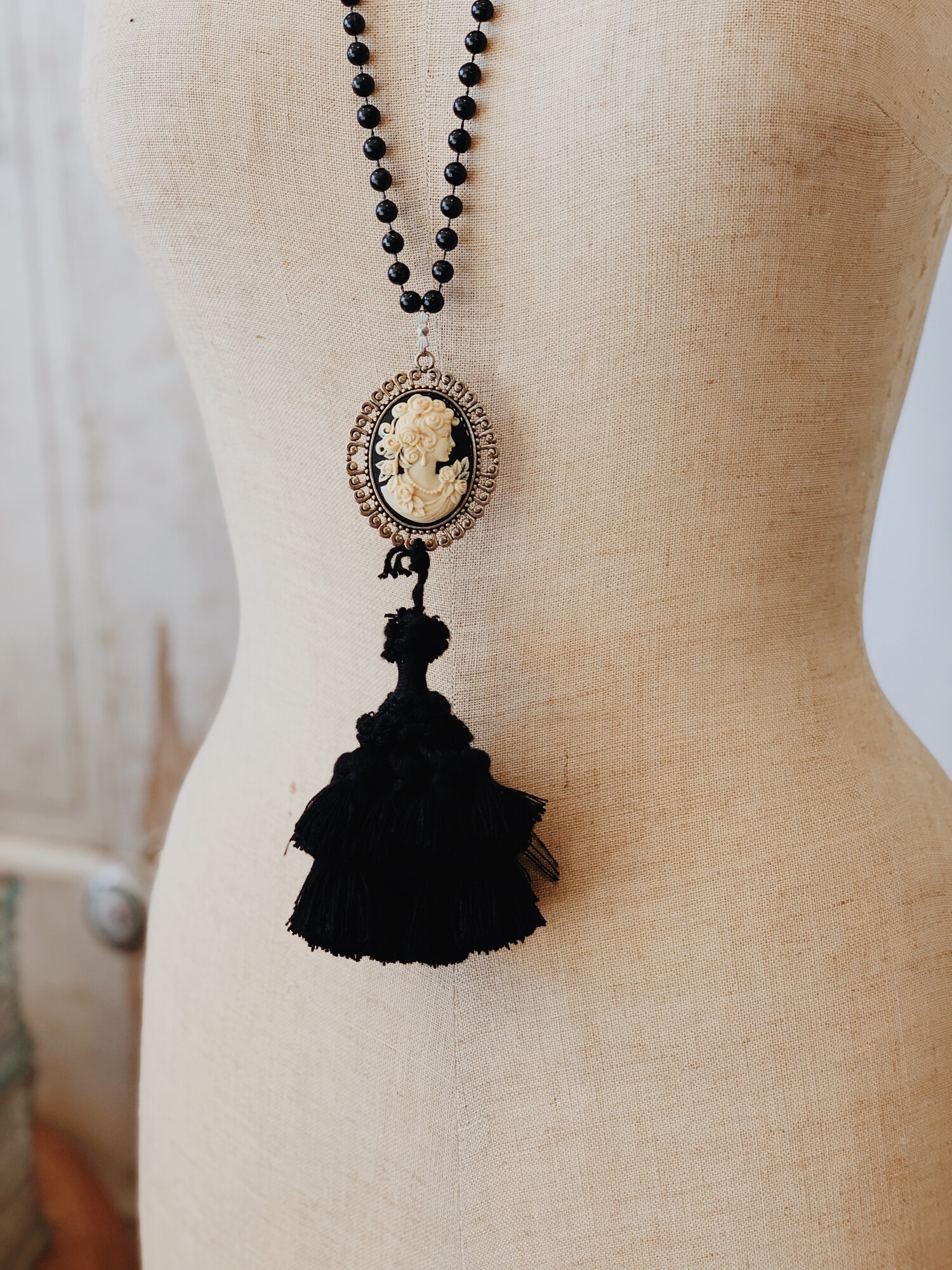 This Kelli Hawk Designs necklace is on a 32 inch strand of beads. The pendant is a beautiful black and cream cameo with a large black tassel attached!