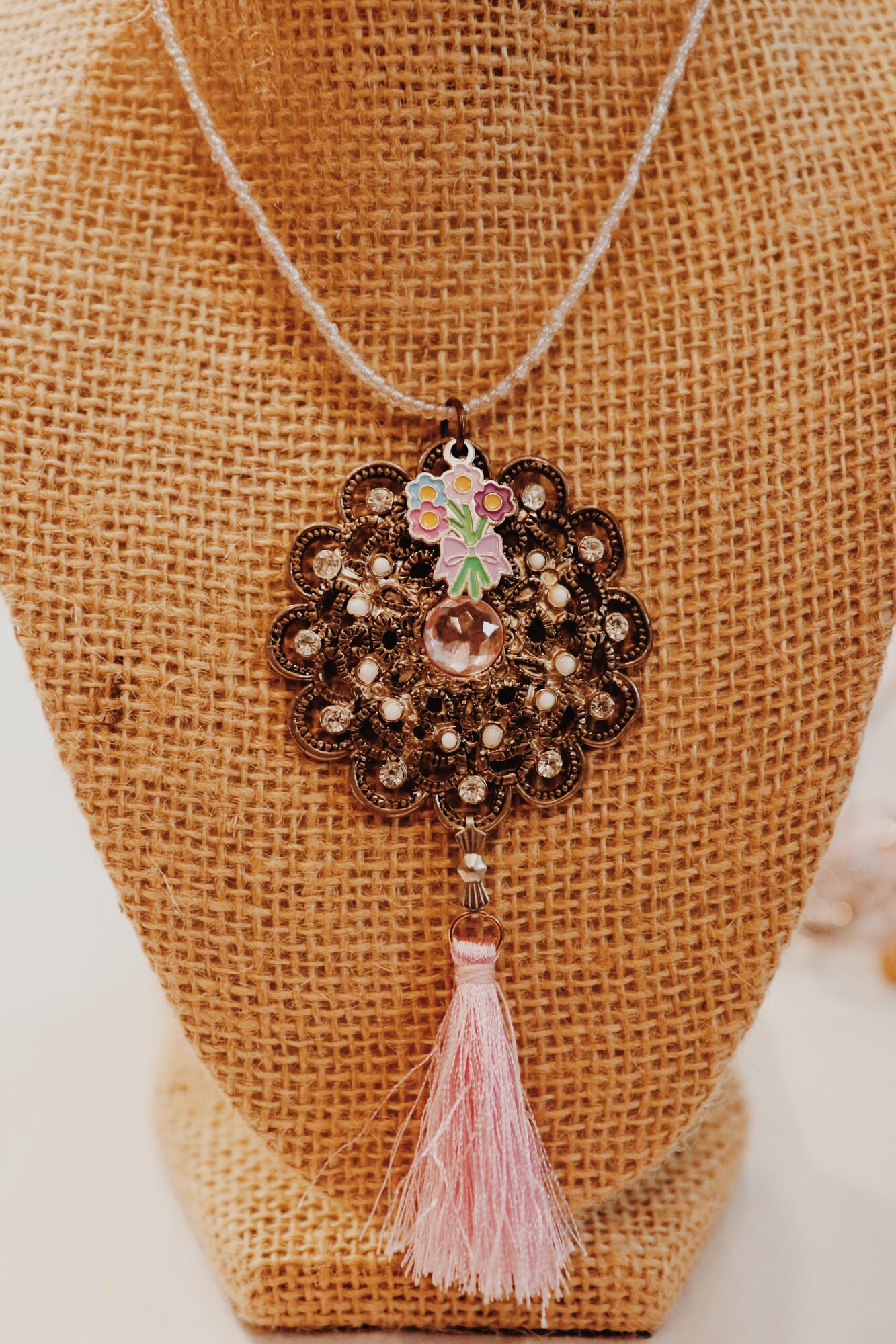 This lovely Kelli Hawk Designs necklace has a vintage broach made to be the pendant with a flower bouquet charm and a pink tassel. It hangs on a 15 inch strand of beads with a 3 inch extender.