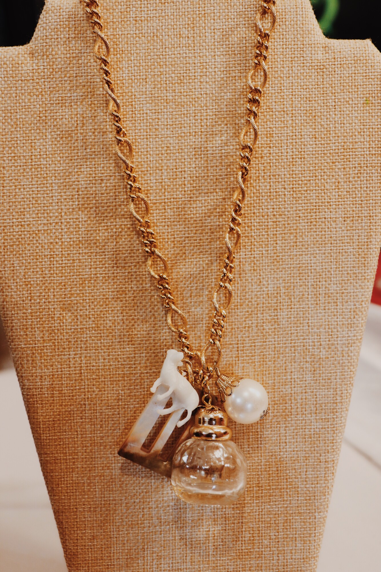 This one of a kind Kelli Hawk Designs necklace has a farm animal, an iridescent buckle, a vintage perfume bottle, and a pearl as the centerpieces. This hangs on a 18 inch chain.