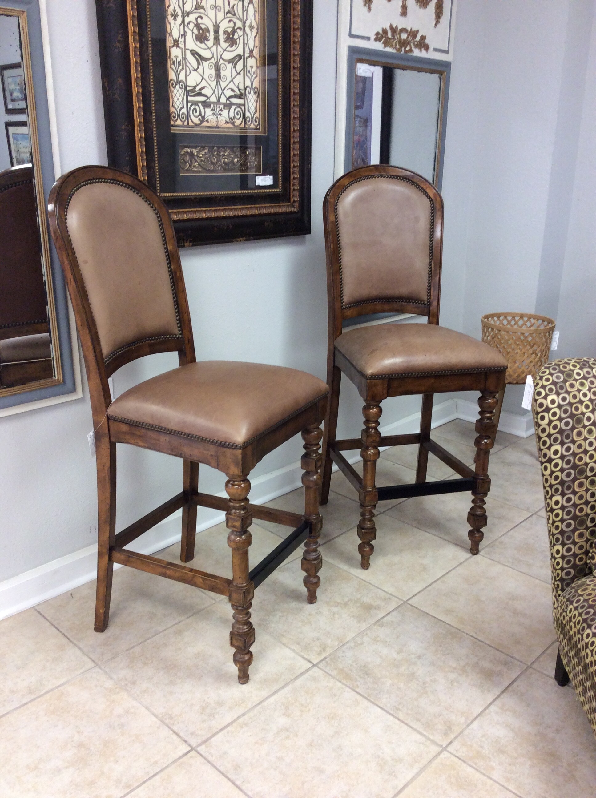 This is a gorgeous pair of barstools by Bernhardt Furniture. Rustic in style, they are solid and well-made. They feature a dark wood finish with lovely carved details. Distressing has been added for that timeless, weathered look that is so popular and even more so withTexas Rustic. The leather upholstered seats are delish, soft and supple in a light brown. All finished off with a bold nailhead trim.