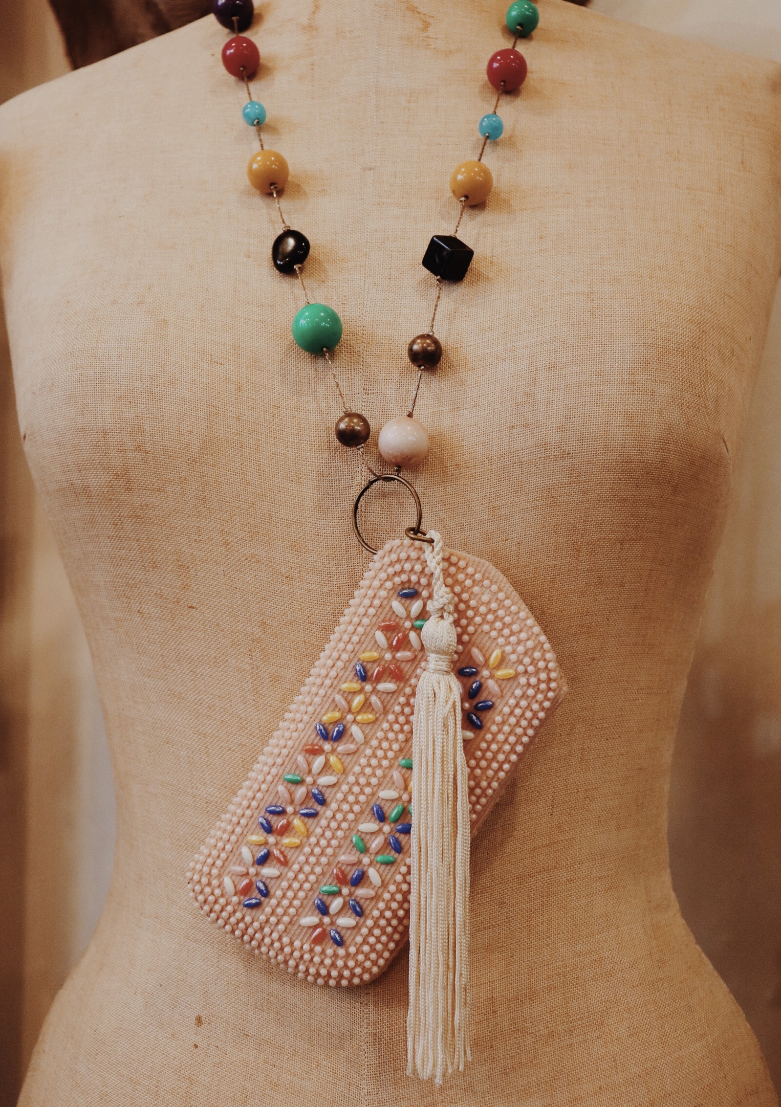 This one of a kin and colorful handmade necklace is on a strand of multicolored beads that measures 30 inches. The centerpiece is a cream colored tassel and a pink beaded pouch!
