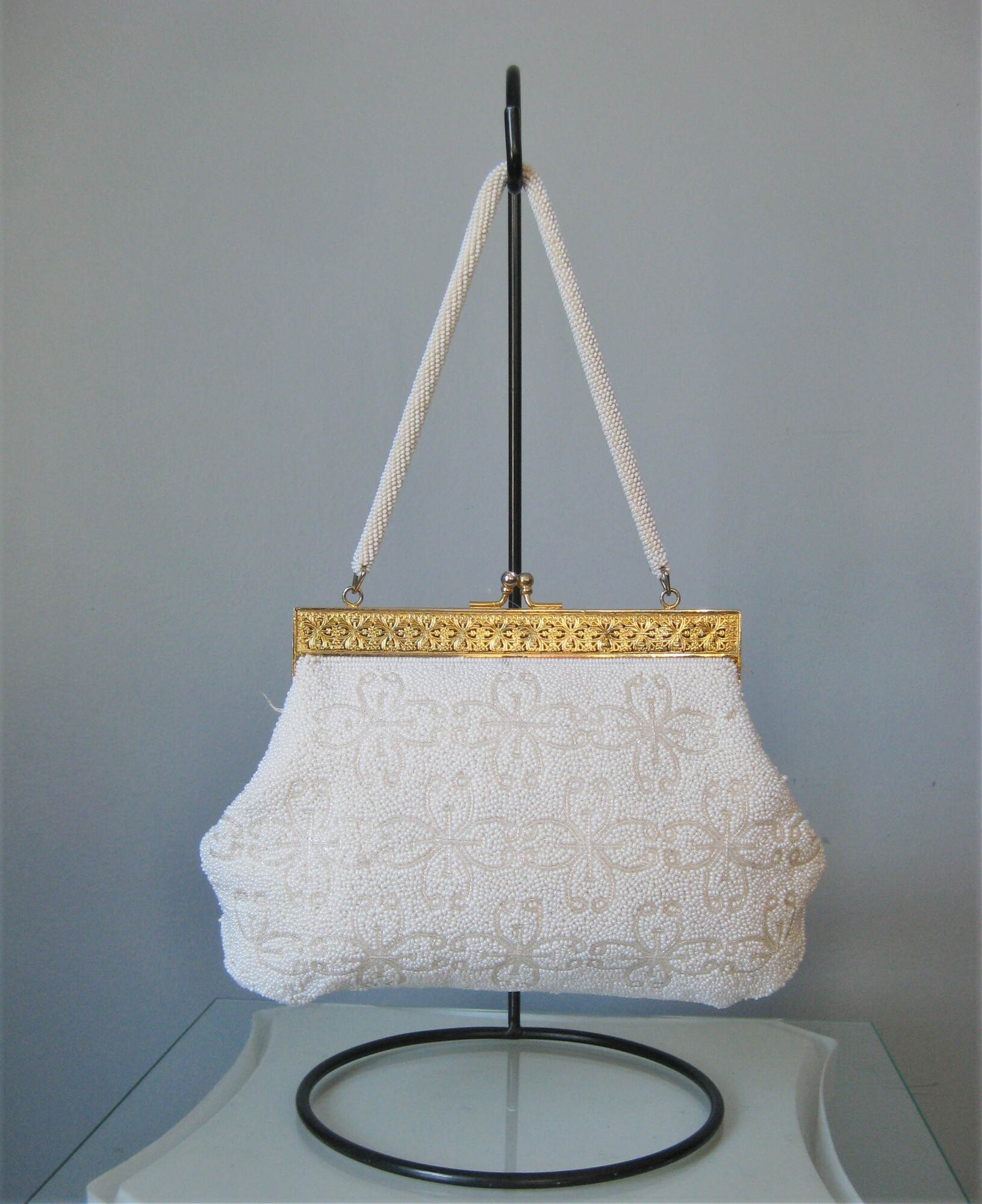 White beaded Frame bag from the 1960s.
high quality gold metal frame with modeled relief and jeweled tilt clasp.
the frame opens wide which is really usefull.  Roomy interior lined with white satin with a few slip pockets.
Single beaded handle.
Made in British Hong Kong by Grande Maison Blanche

Great condition, with some brownness on a few beads on one side and some rust stains on the inside.

Width 7
Height: 6.75
Depth: 1.5
Handle Drop: 5.75
thank you for looking!
#43958