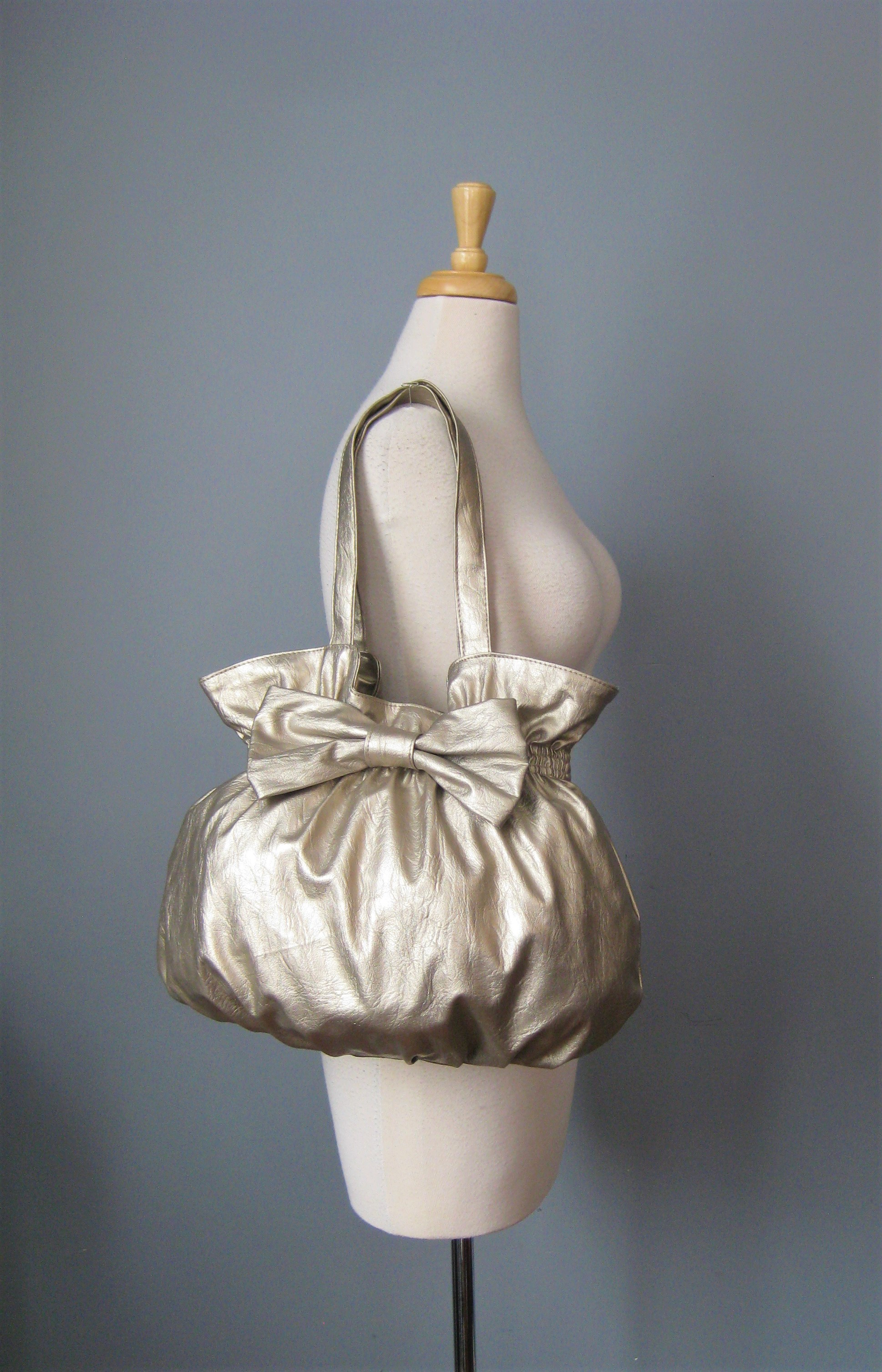 Shimmery Bow Shldr, Silver, Size: None
Super cute and girly, this bag is a large shoulder bag in pale gold metallic vinyl.
It has a pouch shape with a large bow on the front.
Two nice wide straps, magnetic snap closure
lined in light colored fabric with 1 zippered pockets and 2 slip pockets.

No brand ID tag.
Pristine!

thanks for looking1
#41885