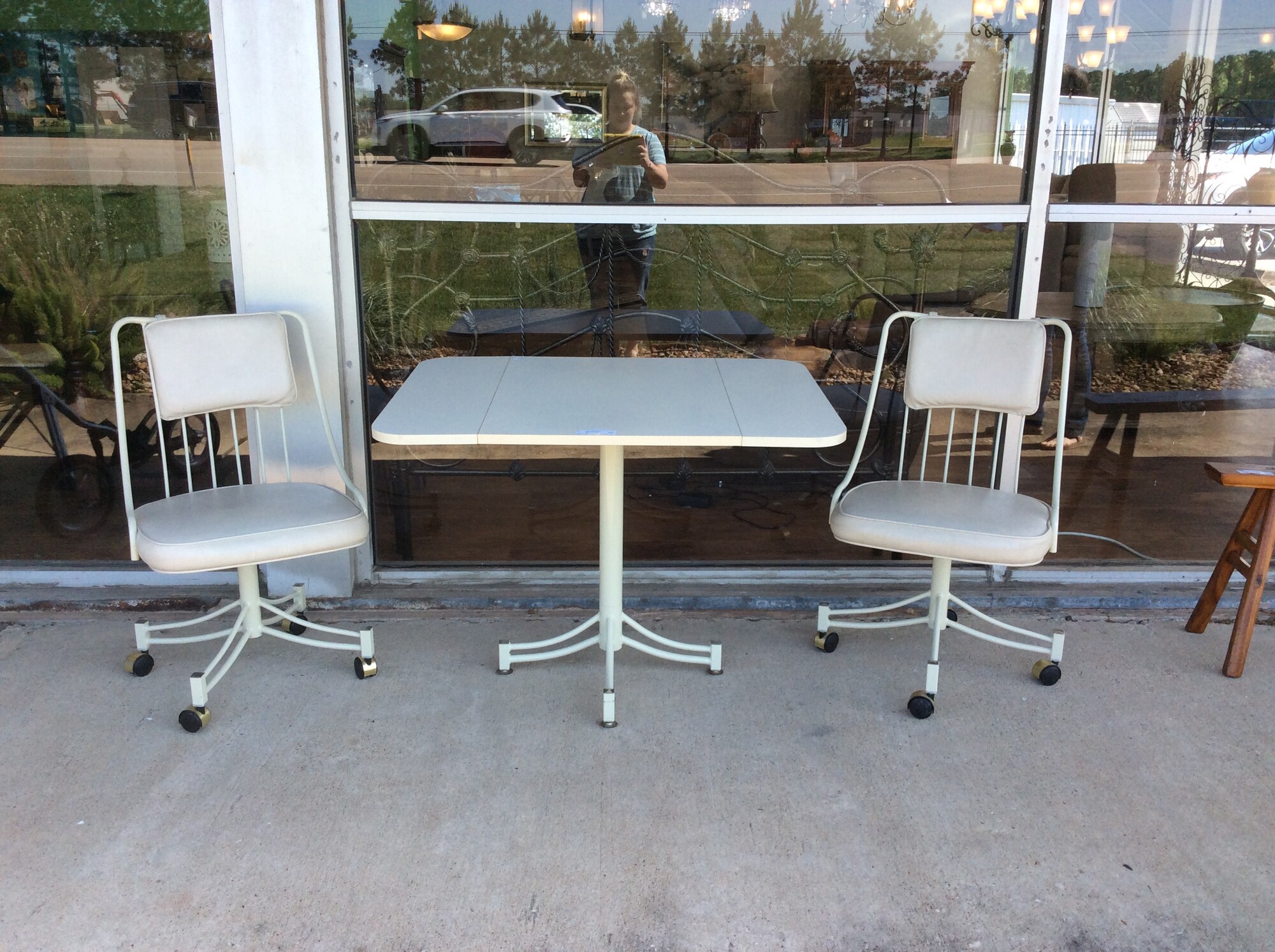 White Metal Table with a wood top and 2 drop leafs on bothsides of the table. This table includes 2 white metal rolling chairs with white detachable cushions.