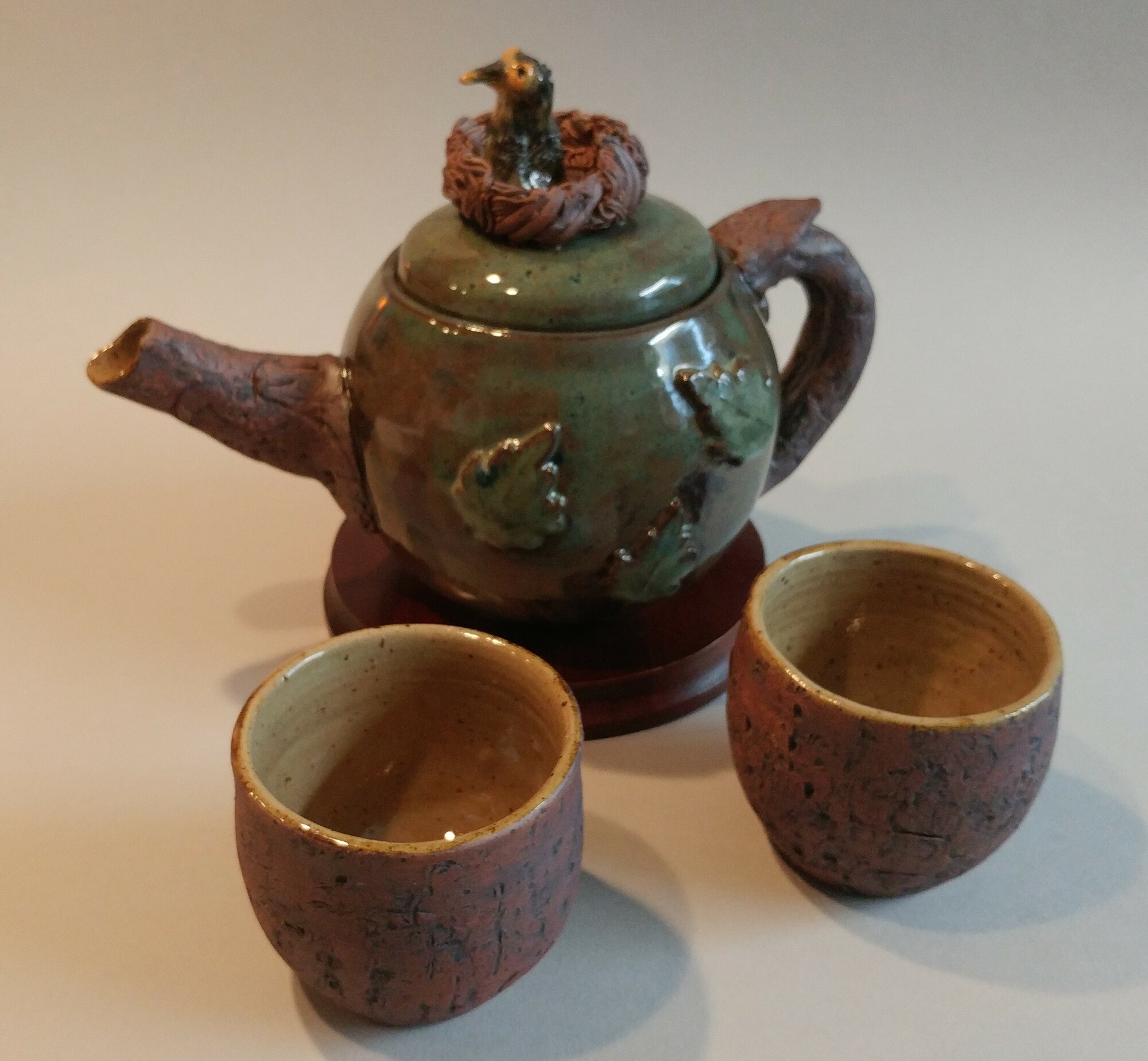 Birdnest Teapot Set
Artist:  Pam Gray
Medium:  Pottery
Dimensions:   teapot is 10 in. length, 6 in wide, and 7 in tall; cups are  3-1/2 in x 3 in.
Description:  Stoneware 12 cup  teapot with baby bird in nest on lid with 2 matching cups.  Mugs hold 5 oz.   The teapot's handle and spout and the cups are textured with wood pattern.