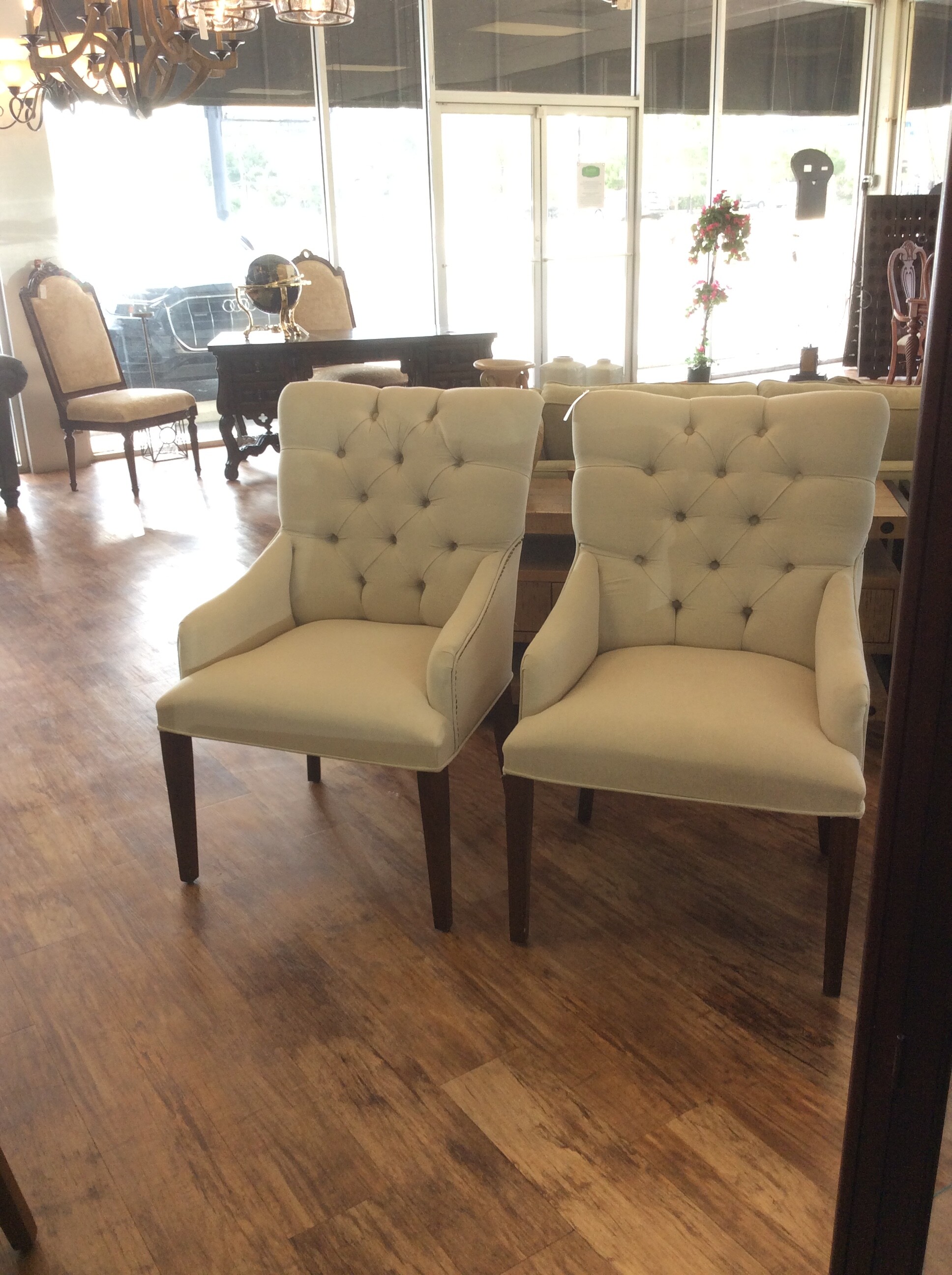 This is a pair of beige, upholsterd, tuffed arm chairs. These chairs have dark brown legs and nailhead trim