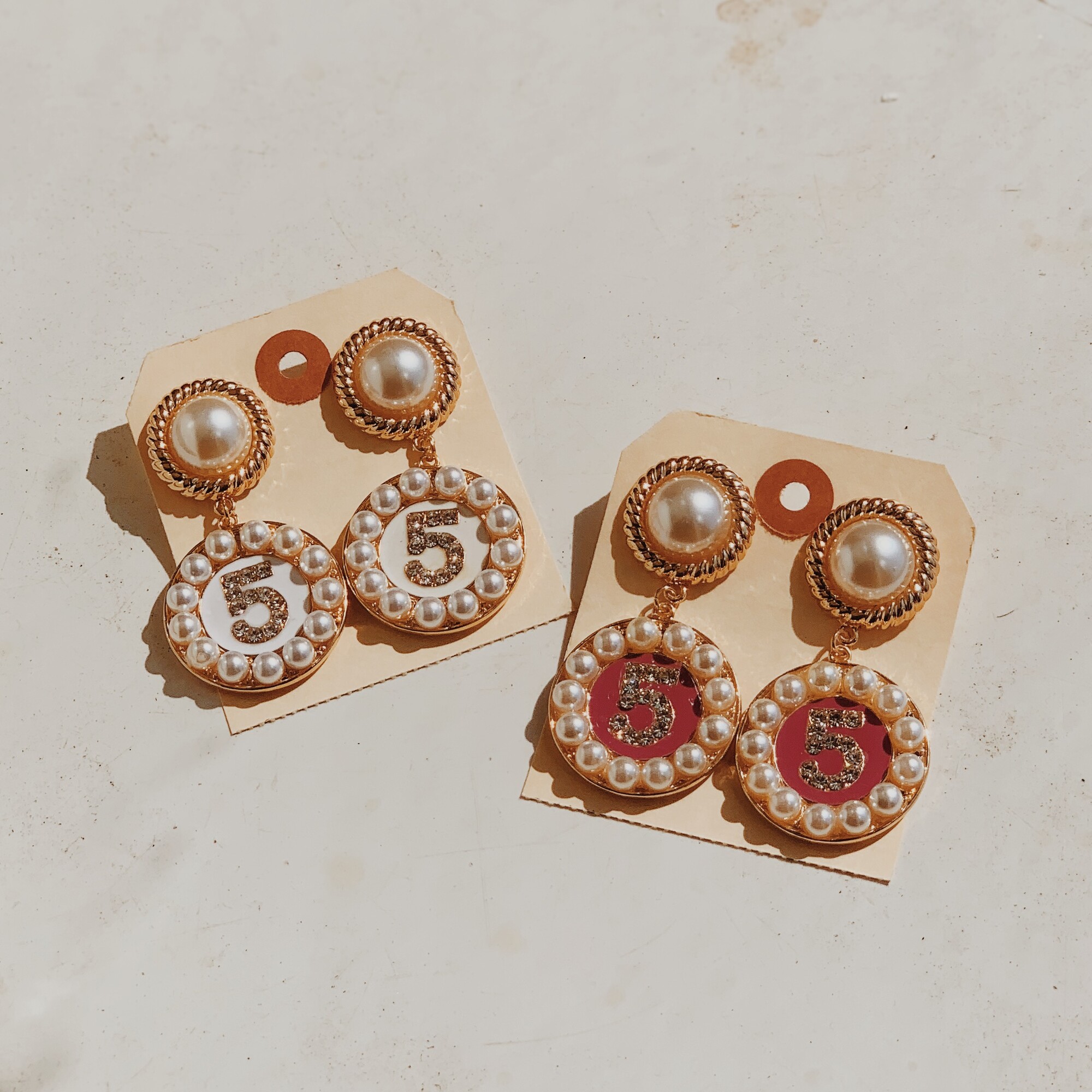 These fun earrings are bedazzled in faux pearls and rhinestones and have the number 5 on them! They measure 2.5 inches in length and are available in white or pink.