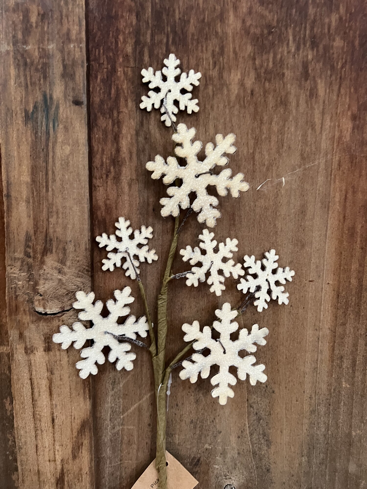 Wooden Snowflake pick is a festive winter floral that has an array of wooden cutout snowflakes on a brown-wrapped floral stem. The snowflakes are heavily coated with glitter for an icy sparkle
Simply place pick in a floral vase or pitcher to complete the look. Measures 13 inches high
