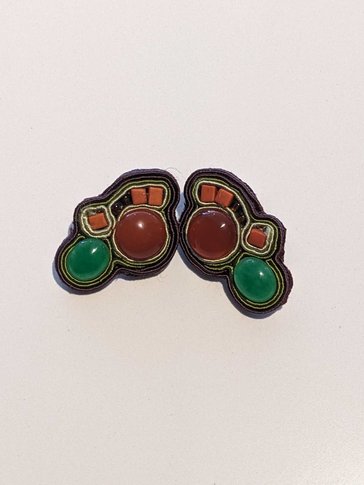 Soutache Earrings
Jama Watts
Jewelry (Soutache)
1.5 in long by 1 in wide
Chalcedony and carnelian cabochons surrounded by green and brown soutache ribbon with terra cotta and copper glass beads.  Backed with maroon ultrasuede. Stainless steel posts.