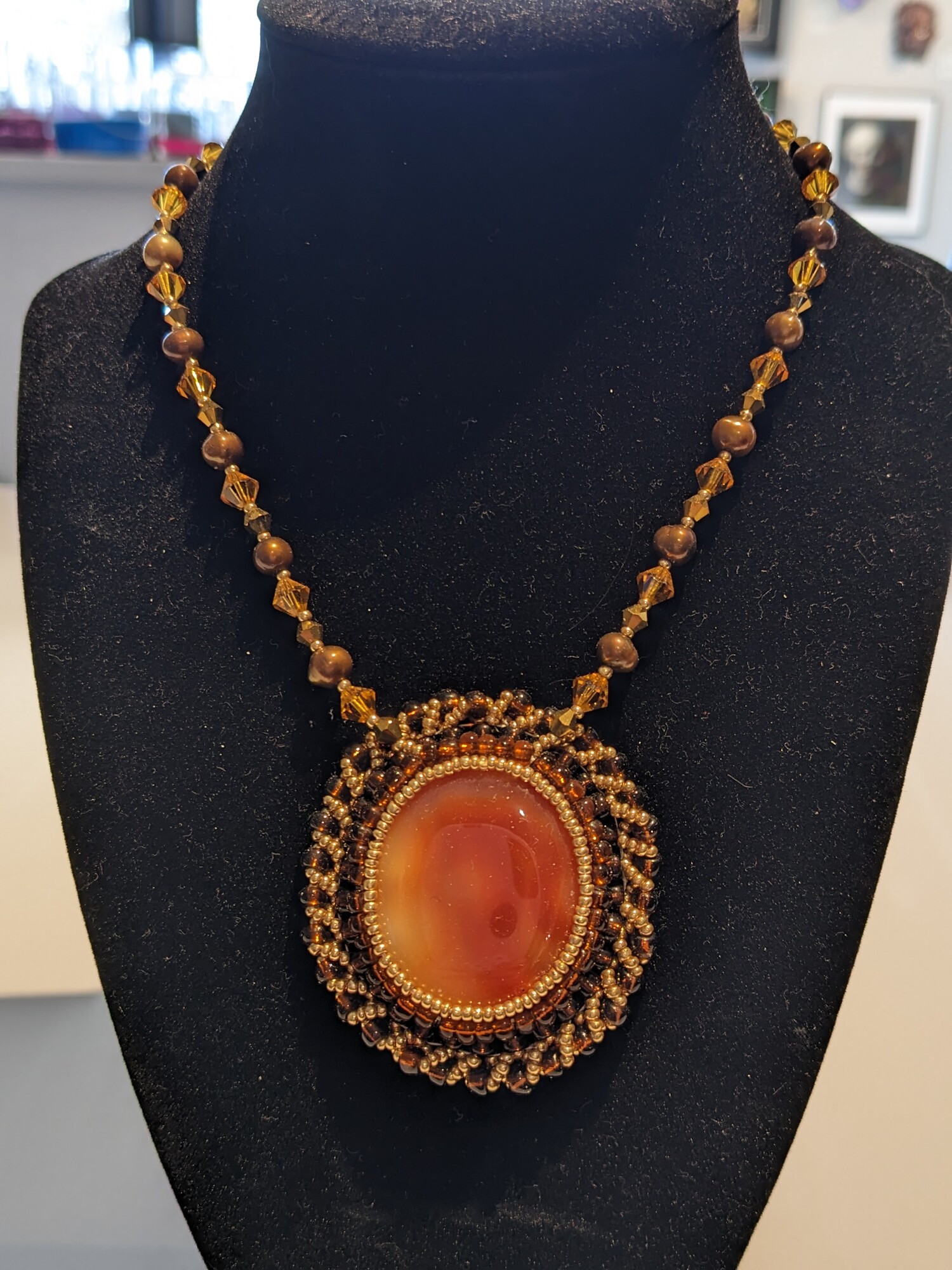 Carnelian Pearl Necklace
Jama Watts
Jewelry (Bead Embroidery)
18 in length, pendant measures 2.25 in length by 2 in wide
Large carnelain cabochon surrounded by copper and gold seed beads and strung on a chain with pearls and leaded glass crystal. Pendant is backed with tan ultrasuede.  Chain ends in a brass lobster clasp.