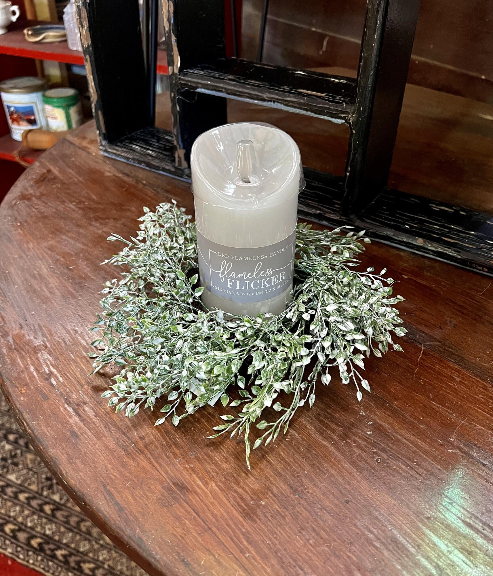 Little Luna Candle Ring has a grapevine base with stems of mini green leaves, accented with white, attached to the base. Ring has a 3 inch diameter and a 10 inch outside diameter. Use it around a candle or as a mini wreath accent on a wall or shelf groupings