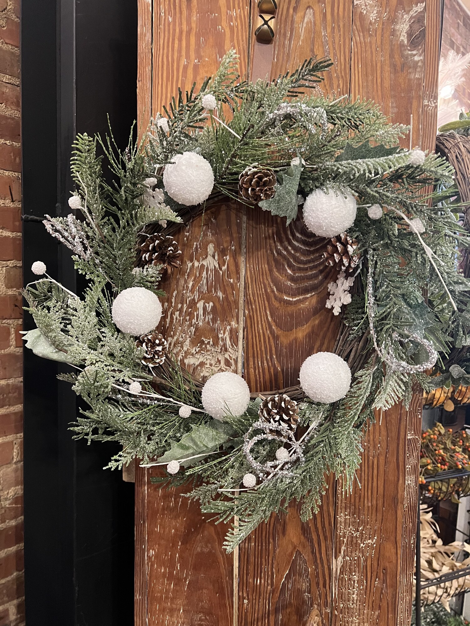 The White Christmas Wreath is the perfect wreath for a warm and inviting wintertime display. Freaturing artificial florals set on a natural grapevine base this wreath has been coated in glistening glitter for a snowy appearance. It is accented by pinecones, styrofoam balls and wooden snowflakes and will look charming in an entryway or front door. Measures 24 inches in diameter