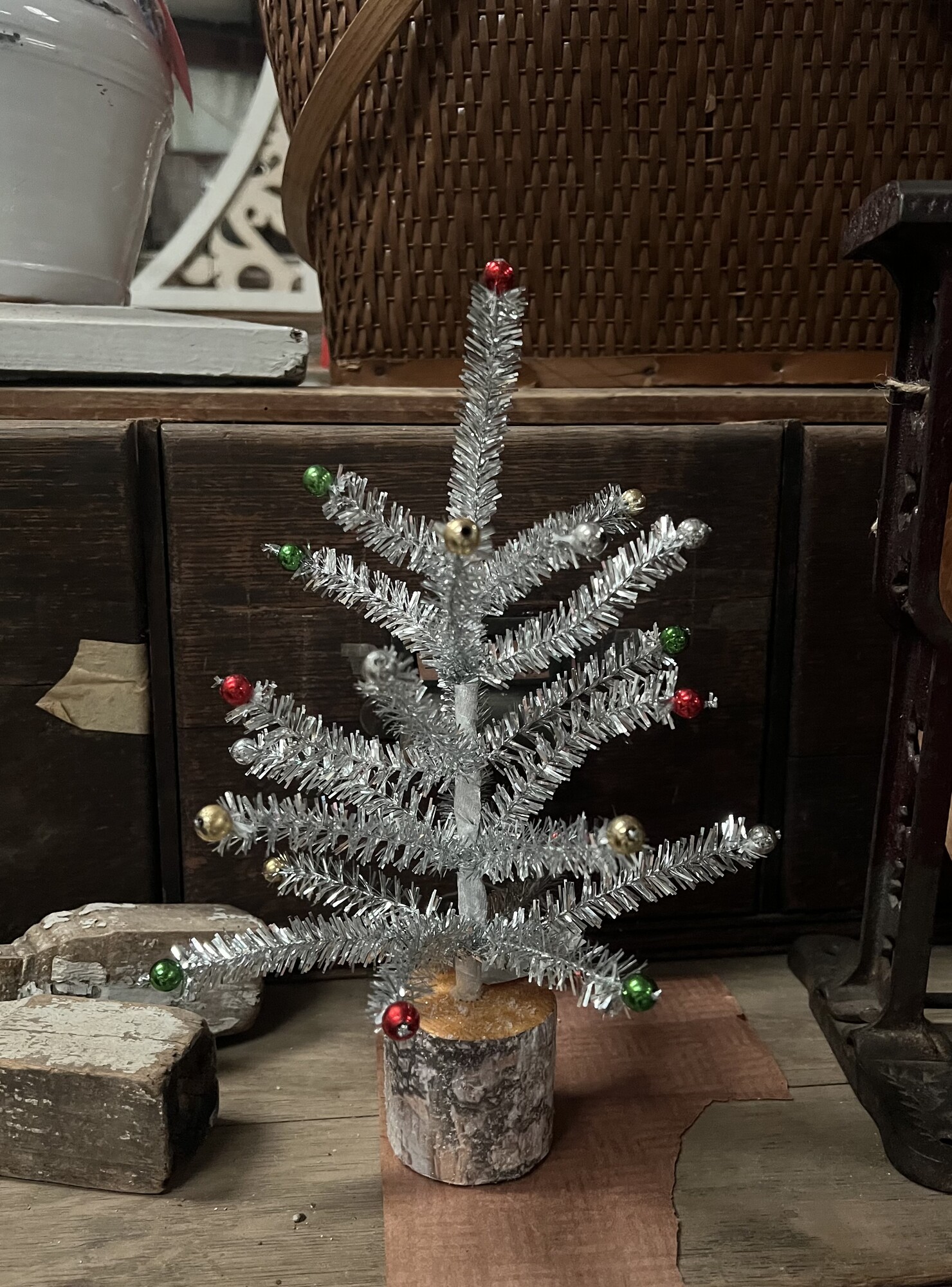 The Silver Tinsel Tree is a table top tree that features a paper wrapped base and silver tinsel foliage. Tree jis accented by red, green and gold baubles.
Tree measures 12 inches high