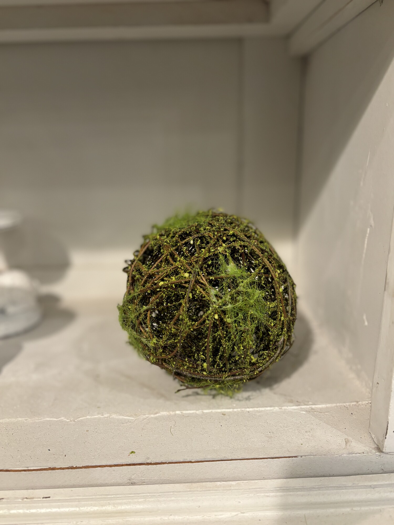 The mossy twig ball is a decorative orb made of natural brown twig material. The sphere is covered in patchy green moss detailing a woodsy look. This ball is perfect for an bowl or tray filler or on top a shelf or stack of books. Measures 5 inches in diameter